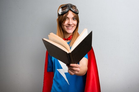 Pretty superhero girl reading book on a gray textured backgroundの写真素材