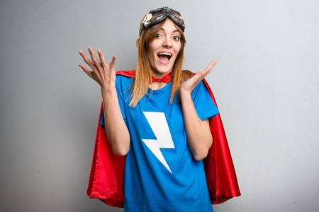 Pretty superhero girl making surprise gesture on a gray textured backgroundの写真素材