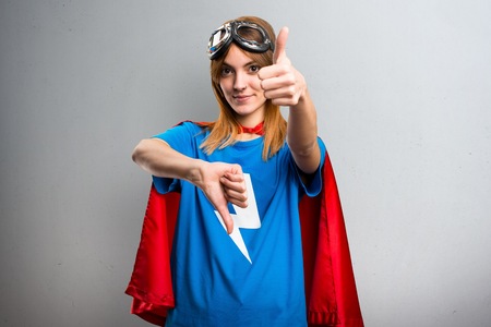 Pretty superhero girl making good-bad sign on a gray textured backgroundの写真素材