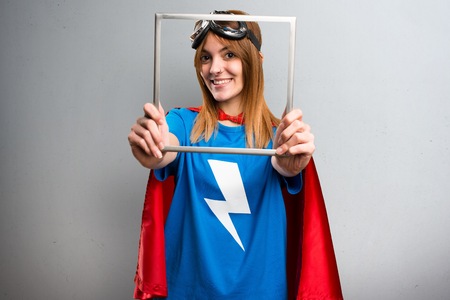 Pretty superhero girl looking through an iron frame on a gray textured backgroundの写真素材