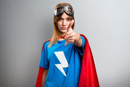 Pretty superhero girl making gun gesture on a gray textured backgroundの写真素材