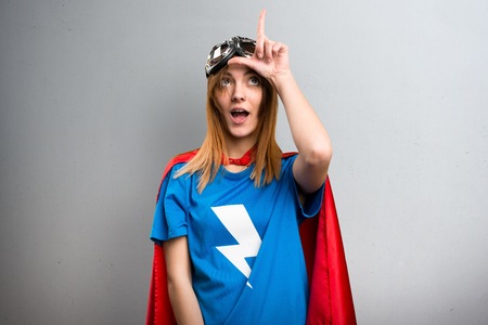 Pretty superhero girl making loser sign on a gray textured backgroundの写真素材