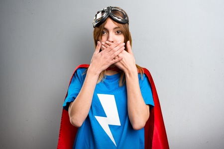 Pretty superhero girl covering her mouth on a gray textured backgroundの写真素材