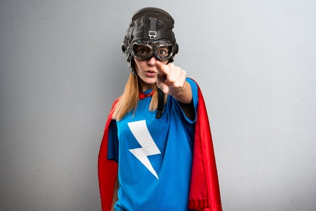 Pretty superhero girl pointing to the front on a gray textured backgroundの写真素材