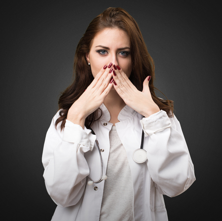Doctor woman covering her mouth on black backgroundの写真素材