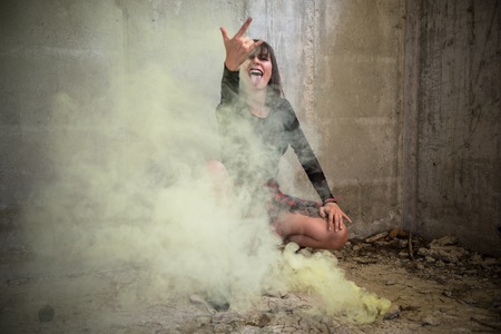 Beautiful young girl with smoke bomb in an abandoned building making rock gestureの写真素材