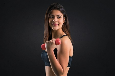 Young sport girl making weightlifting on black backgroundの写真素材