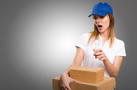 Surprised Delivery woman holding a bulb on grey backgroundの写真素材
