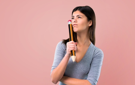 Teenager girl holding a big pencil on pink backgroundの写真素材