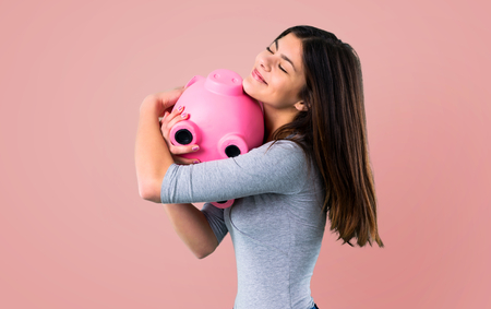 Teenager girl holding a piggybank on pink backgroundの写真素材