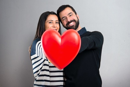 Couple holding a heart toy on grey backgroundの写真素材