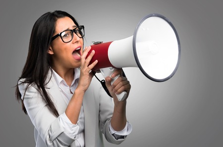 Pretty woman with glasses holding a megaphone on grey backgroundの写真素材