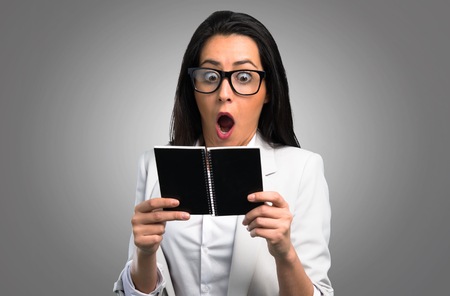 Pretty woman with glasses holding a notebook on grey backgroundの写真素材