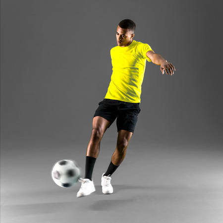 Soccer player man with dark skinned playing kicking the ball on dark backgroundの写真素材