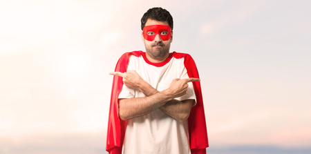 Superhero man with mask and red cape pointing to the laterals having doubts. Undecided person on a sunset backgroundの写真素材