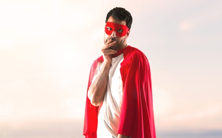 Frightened superhero man with mask and red cape on a sunset backgroundの写真素材