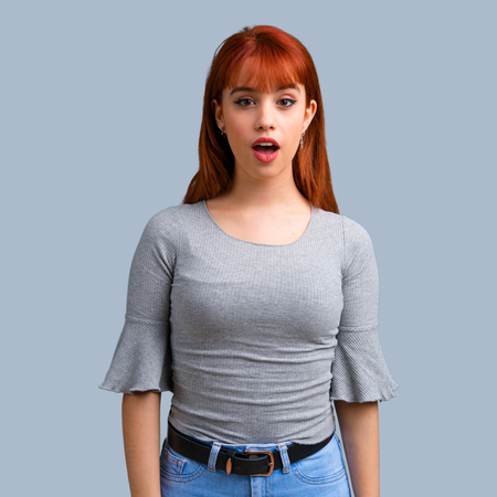 Young redhead girl with surprise and shocked facial expression on blue backgroundの写真素材