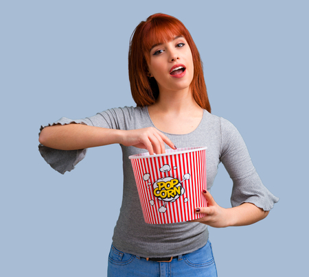 Young redhead girl eating popcorns on blue backgroundの写真素材