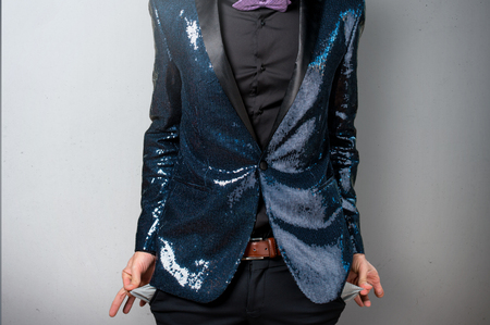 Ruined handsome man with sequin jacket looking money in their pockets on grey backgroundの写真素材