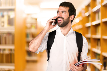Student man with mobile on defocused libraryの写真素材