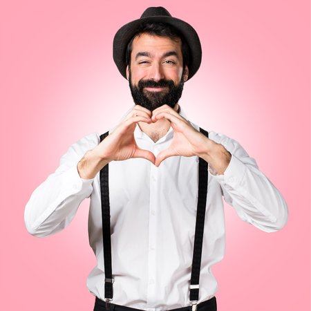 Hipster man with beard making a heart with his hands on colorful backgroundの写真素材
