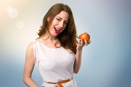 Slim woman with tape measure and holding an apple on blue abstract backgroundの写真素材