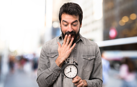 Surprised Handsome man with beard holding vintage clock at outdoorの写真素材
