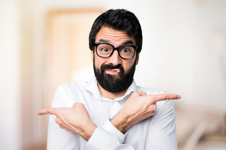 Handsome man with glasses pointing to the laterals having doubts on unfocused backgroundの写真素材