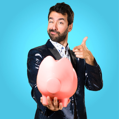 Man with jacket holding a piggybank on colorful backgroundの写真素材