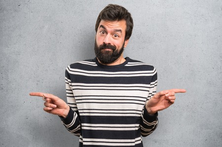 Man with beard pointing to the laterals having doubts on textured backgroundの写真素材