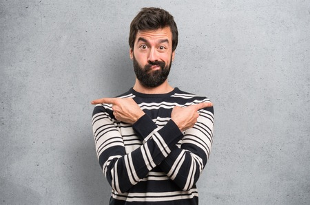 Man with beard pointing to the laterals having doubts on textured backgroundの写真素材