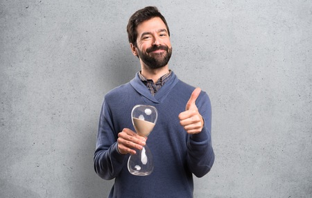 Happy Handsome brunette man with beard holding a sand clock on textured background
