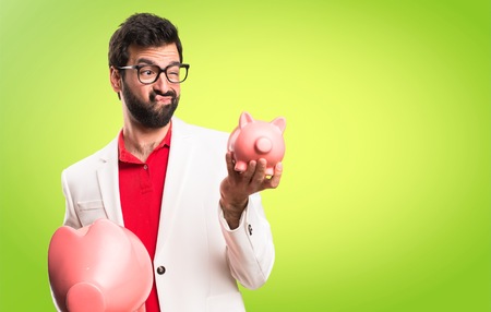 Brunette man with glasses holding a piggybank on colorful backgroundの写真素材