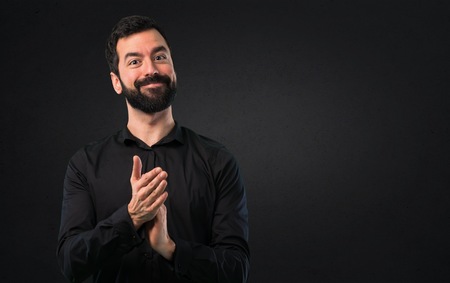 Handsome man with beard applauding on black backgroundの写真素材