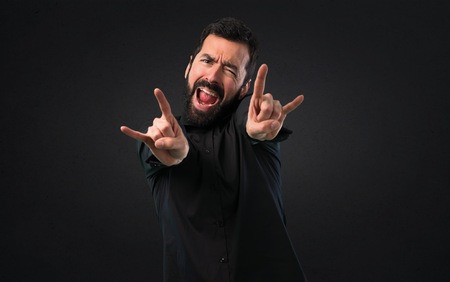 Handsome man with beard making rock gesture on black backgroundの写真素材