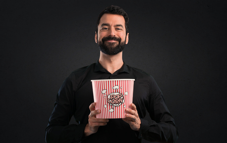 Handsome man with beard eating popcorns on black backgroundの写真素材