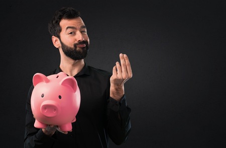 Handsome man with beard holding a piggybank on black backgroundの写真素材