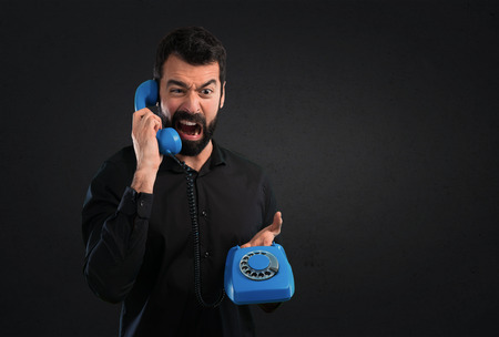 Handsome man with beard talking to vintage phone on black backgroundの写真素材