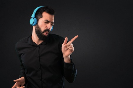 Handsome man with beard listening music on black backgroundの写真素材