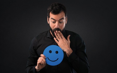 Handsome man with beard holding a happy face icon on black background
