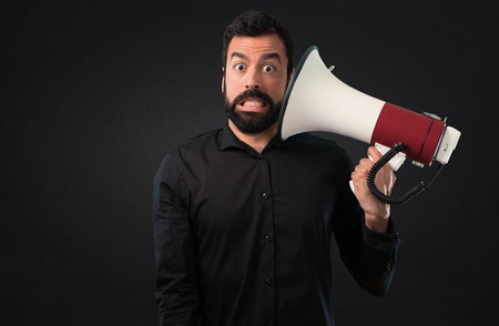 Handsome man with beard holding a megaphone on black backgroundの写真素材