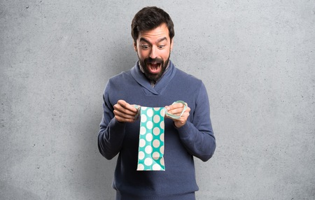 Surprised Handsome brunette man with beard with shopping bag on textured backgroundの写真素材