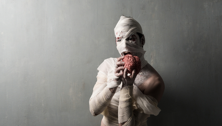 Terrorific mummy eating a brain on textured wall background.  Halloween holidaysの写真素材