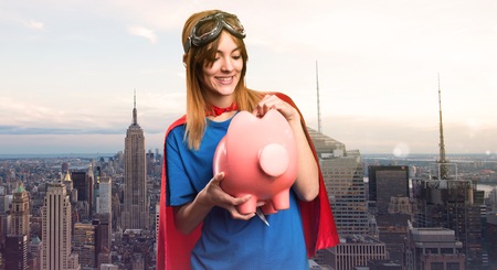 Pretty superhero girl holding a piggybank in a skyscraper cityの写真素材