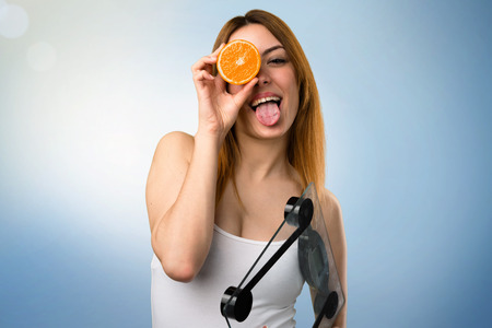 Beautiful young girl with weighing machine holding an orange on unfocused backgroundの写真素材