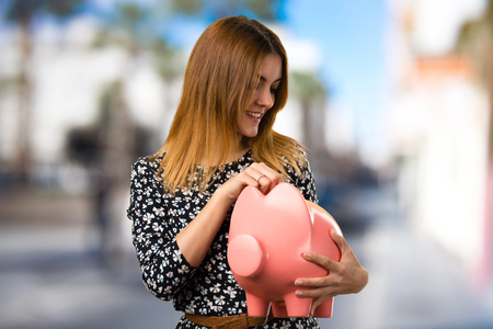 Beautiful young girl holding a piggybank on unfocused backgroundの写真素材