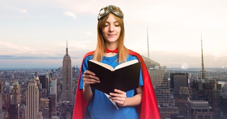 Pretty superhero girl reading book in a skyscraper cityの写真素材