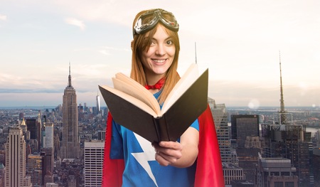 Pretty superhero girl reading book in a skyscraper cityの写真素材