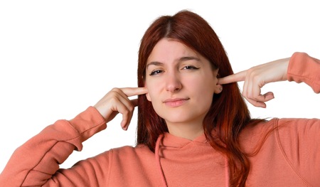 Young redhead girl with pink sweatshirt covering both ears with hands. Frustrated expression on...