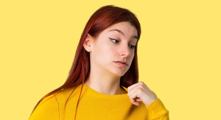 Young redhead girl with yellow sweater with tired and sick expression on isolated yellow backgroundの写真素材